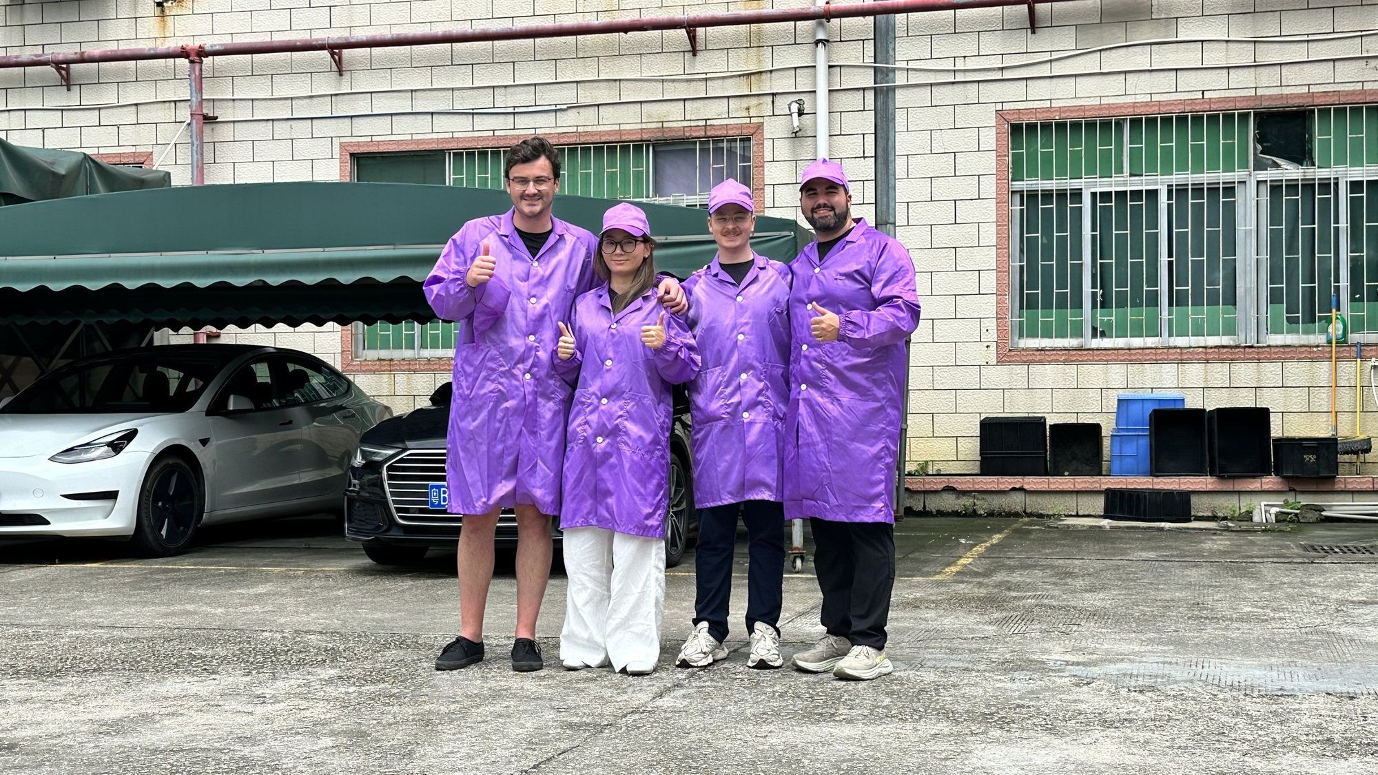 Four people in purple clean-room coats outside a factory building.