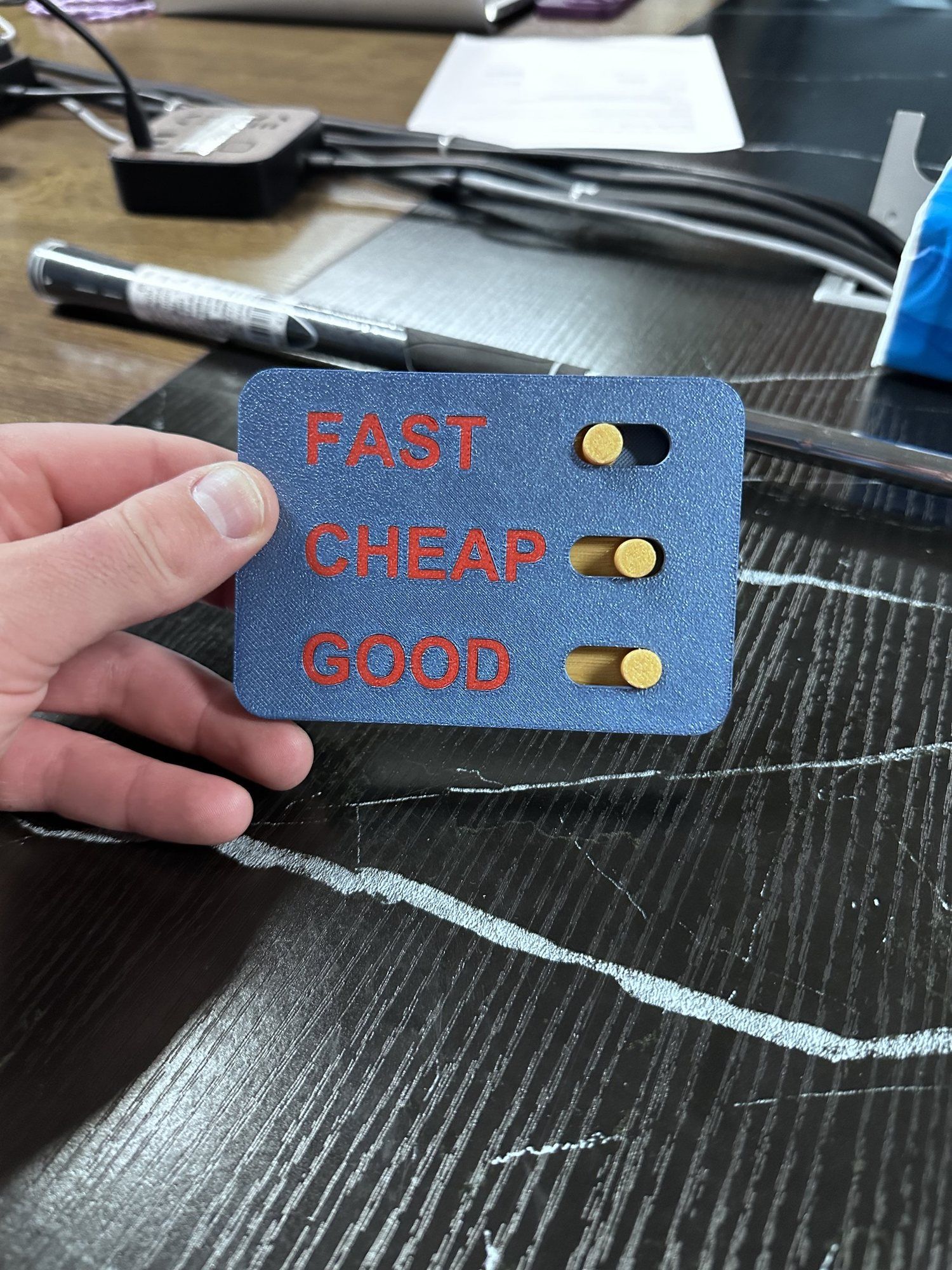 A hand holding a small blue card with three switches labelled fast, cheap and good.