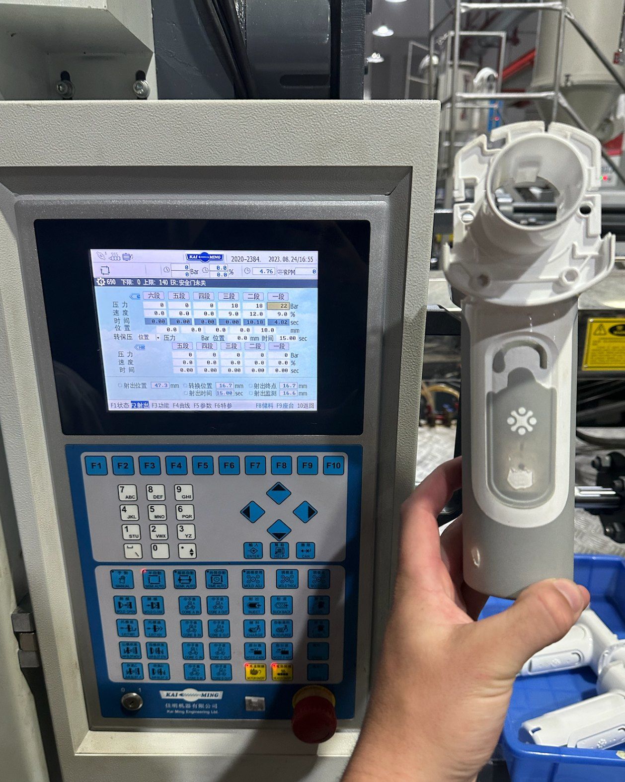 A first moulded part held up beside the press controller screen.