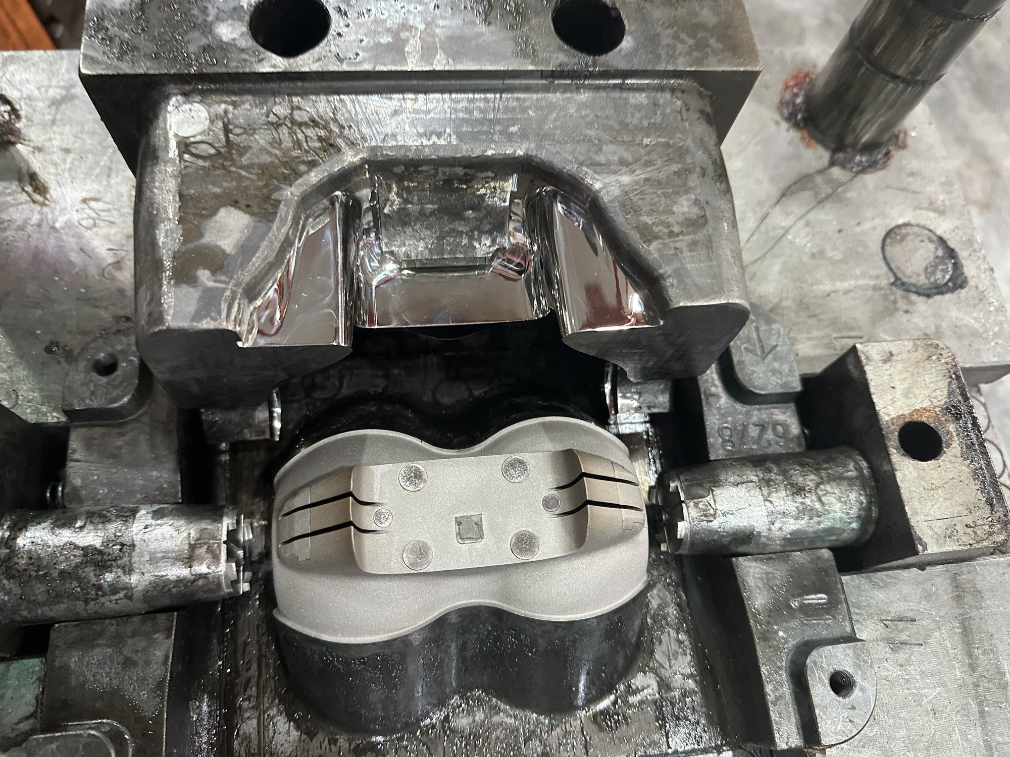 A steel injection mould opened to show a moulded housing in its cavity.