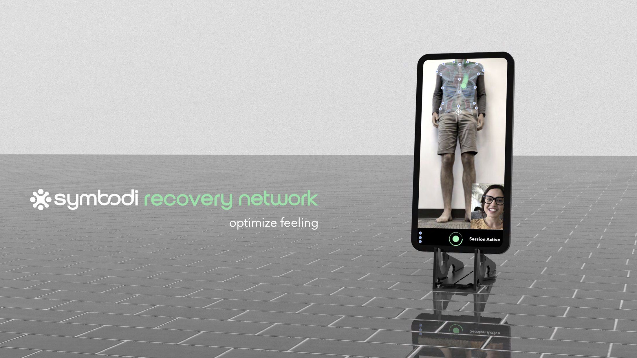 A phone on a small stand showing the Symbodi Recovery Network, with a muscle map over a person standing against a wall and a clinician on a video call.
