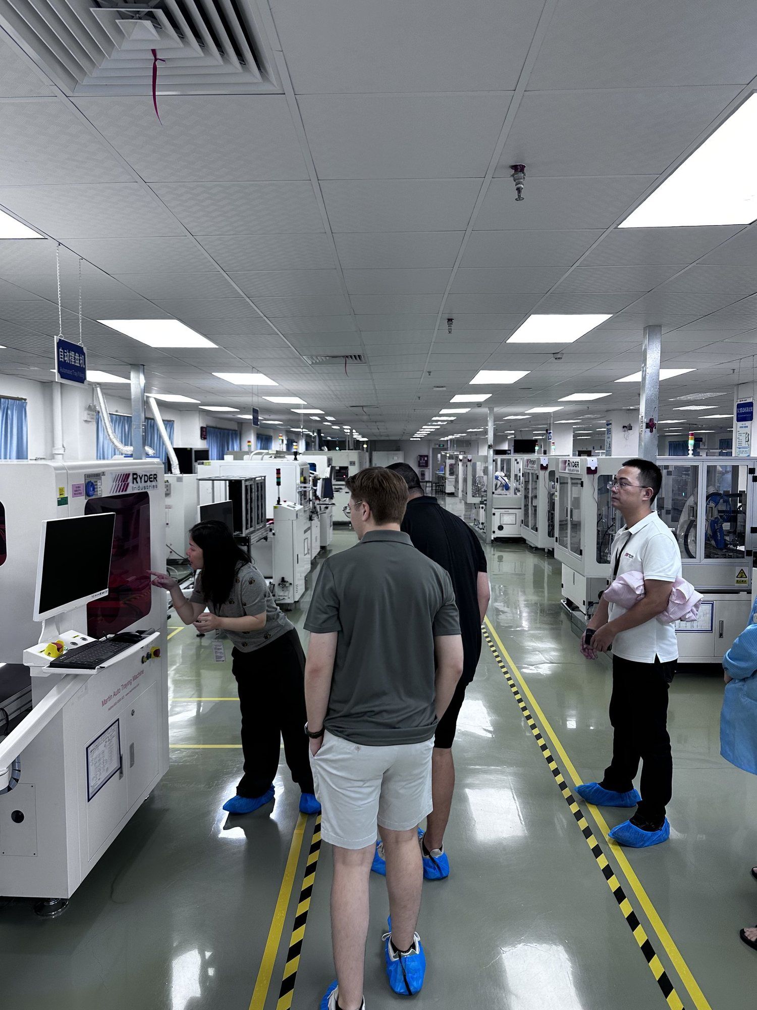 A group in shoe covers walking between circuit board assembly machines.