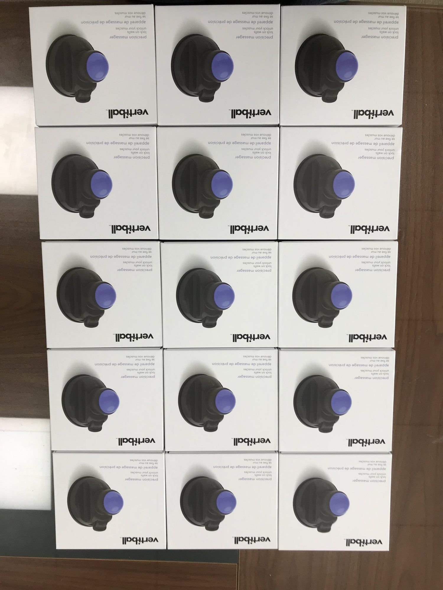 Fifteen boxed Vertiballs laid out in a grid on a factory table.