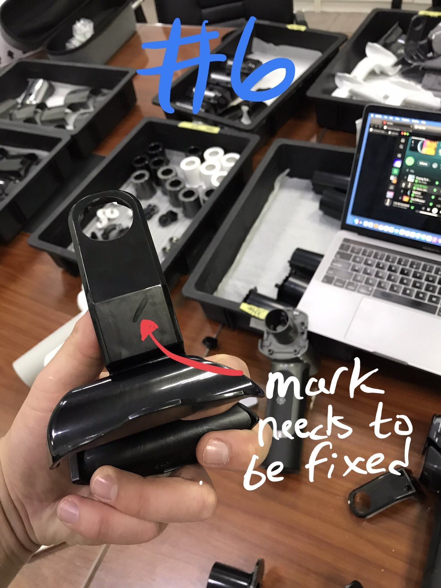 A hand holding a black moulded part, with a note drawn on the photo that the mark needs to be fixed.